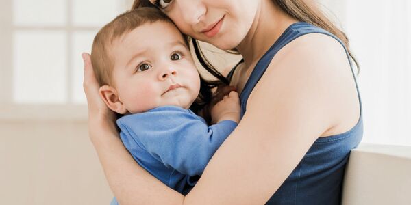 Junge Mutter hält Baby im Arm, blickt zu Betrachter